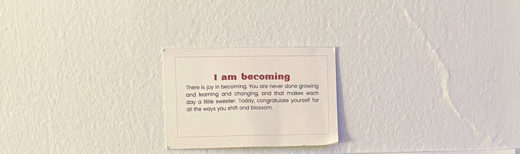 A small card on the wall depicting "I am becoming"